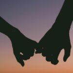 Silhouetted hands holding at sunset over a calm ocean. Romantic and peaceful seascape.
